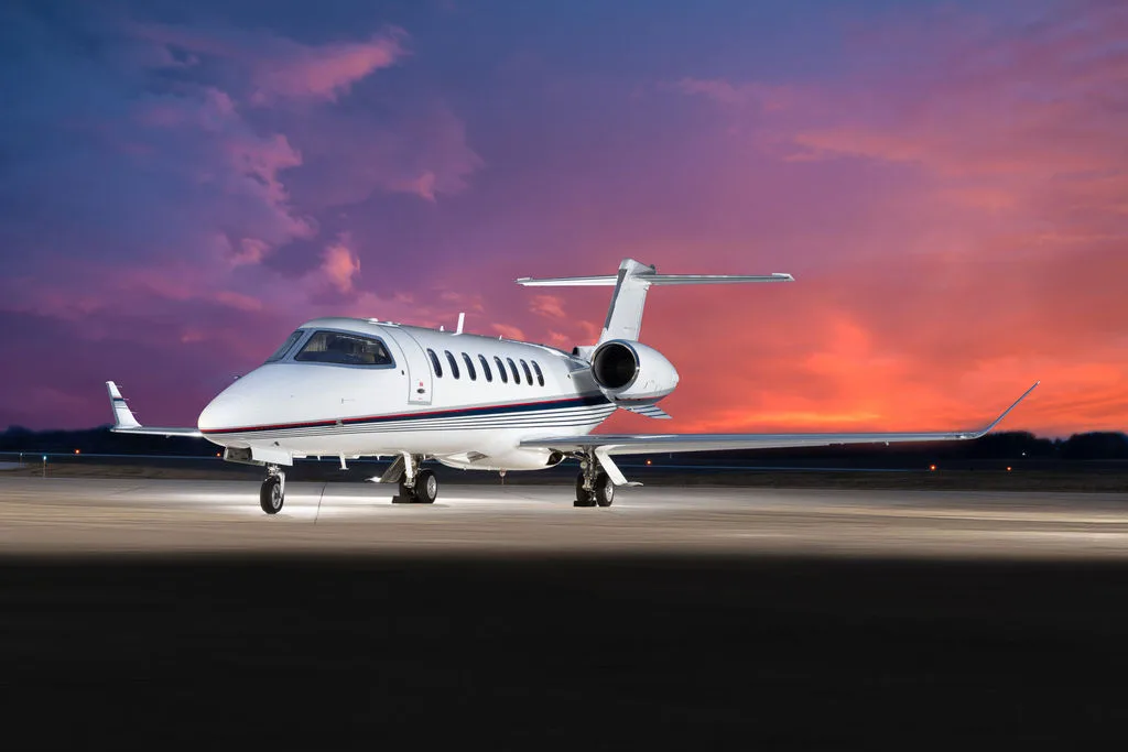 A white business jet with blue and red stripes on the tarmac at sunset.