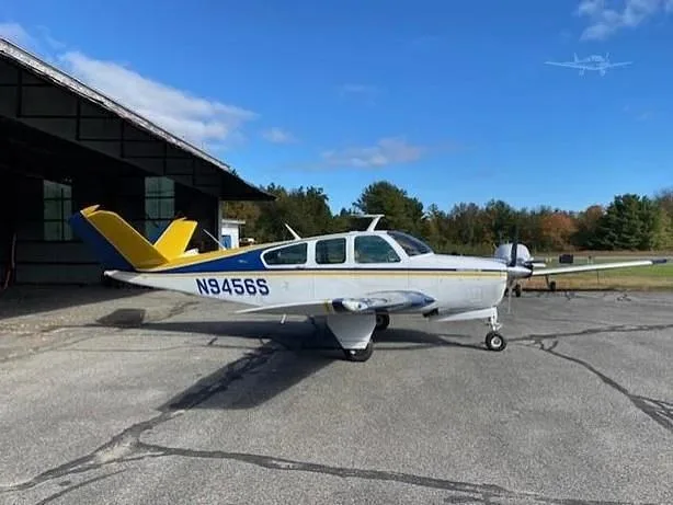 A white single-engine aircraft with blue and yellow tail accents, registration N9456S, parked outside a hangar.