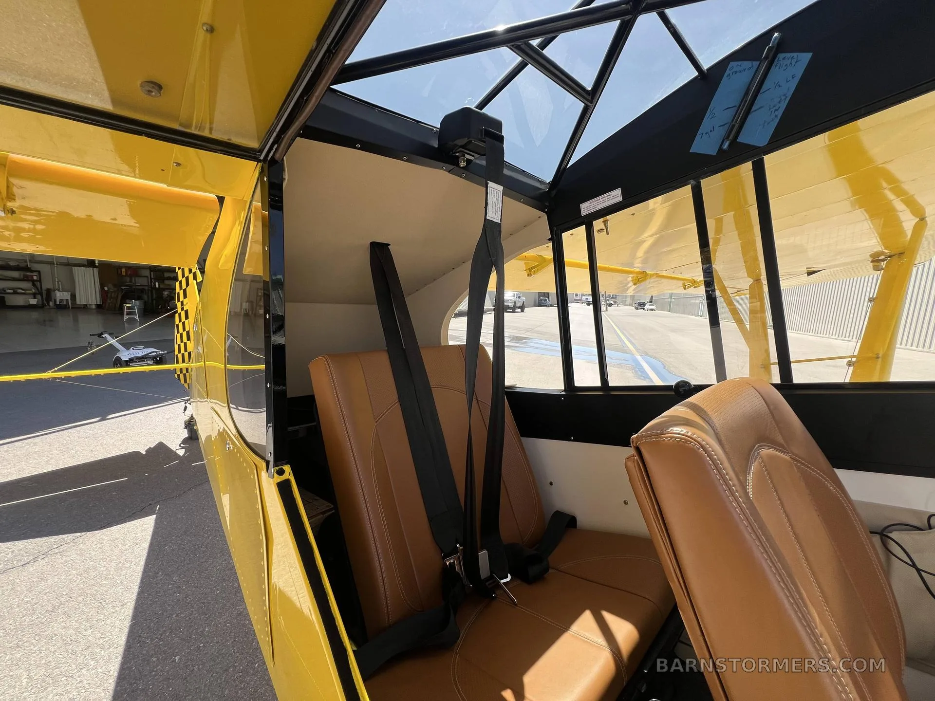 The interior cabin of a yellow experimental aircraft, showing brown leather seats and the overhead structure.
