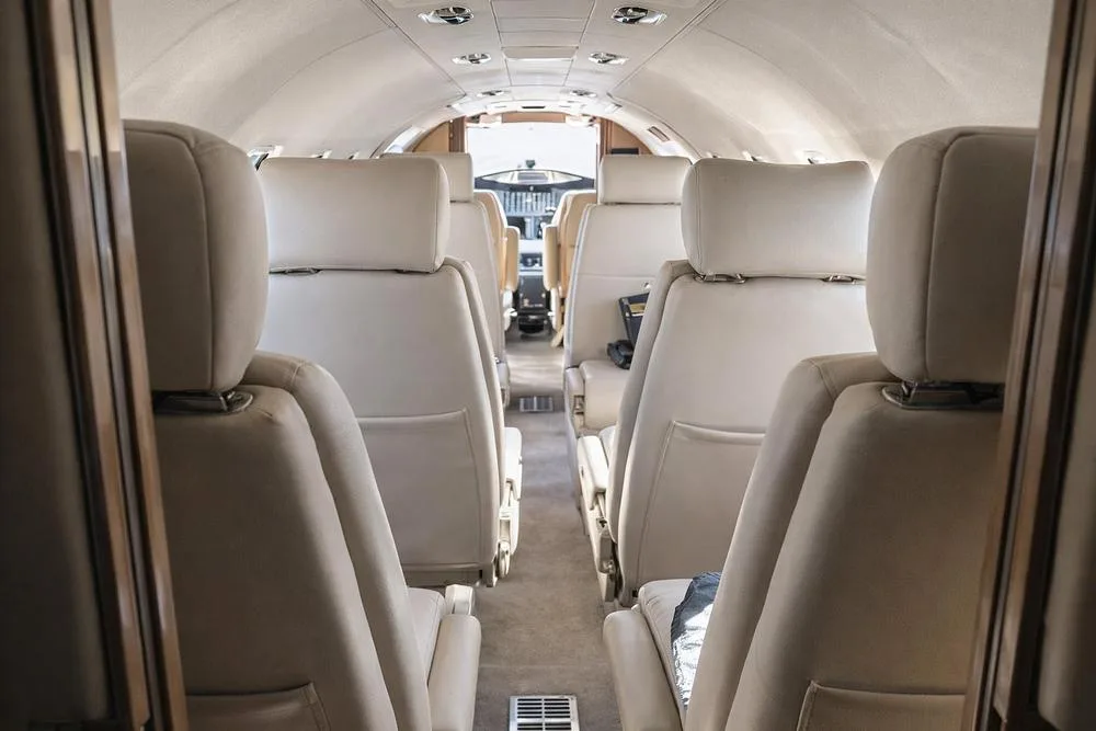 View looking forward down the aisle of a private jet cabin with light-colored leather seats.
