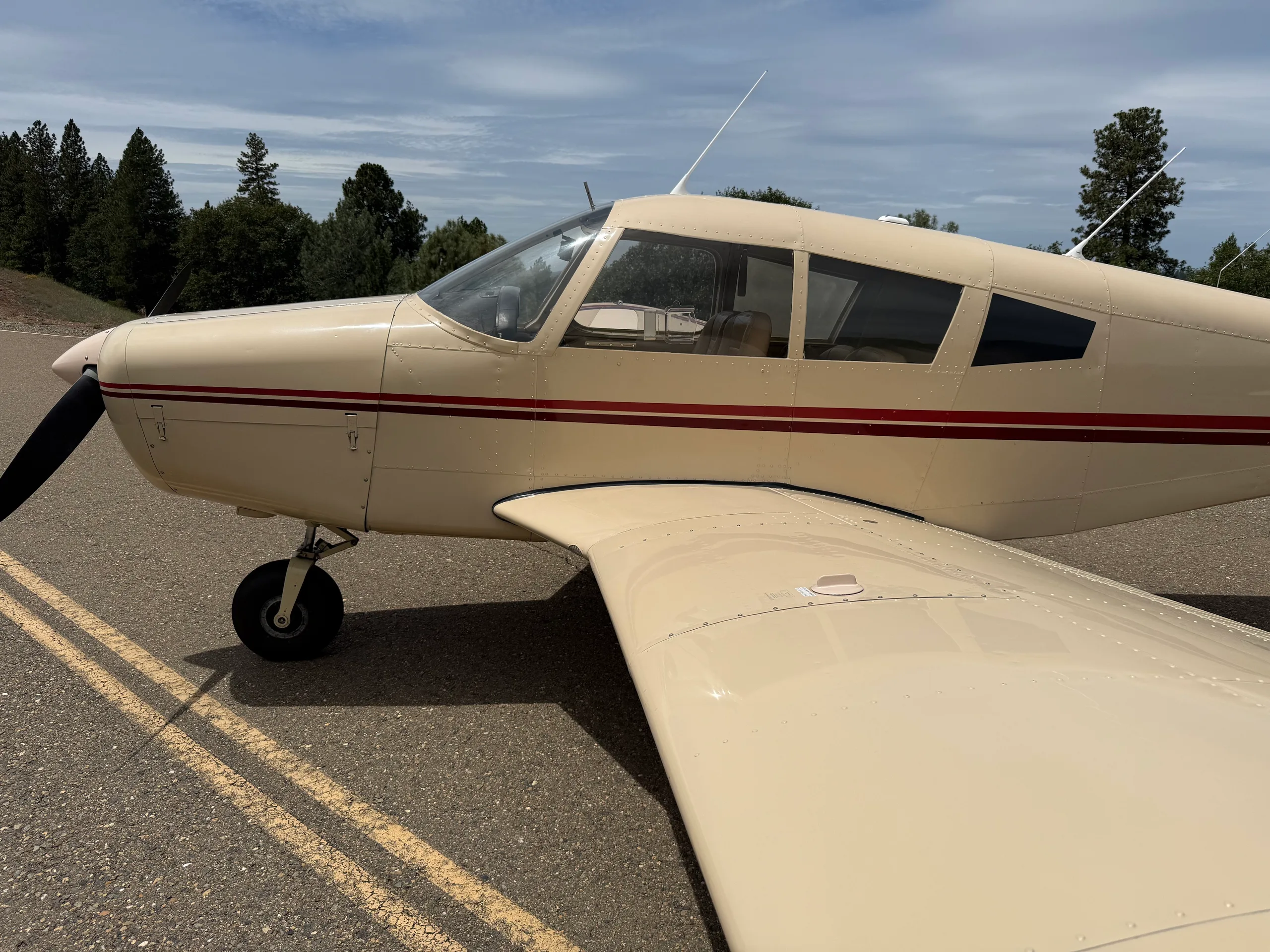Close-up side view of the cream-colored aircraft's cockpit and wing on an asphalt surface.