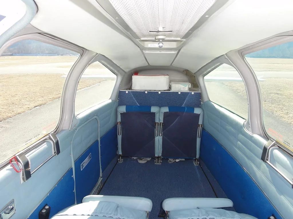 The aircraft's interior cabin looking towards the rear, showing blue and light grey seats, a cooler, and large windows.