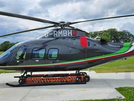 A gray helicopter with red and green stripes sits on a concrete pad.