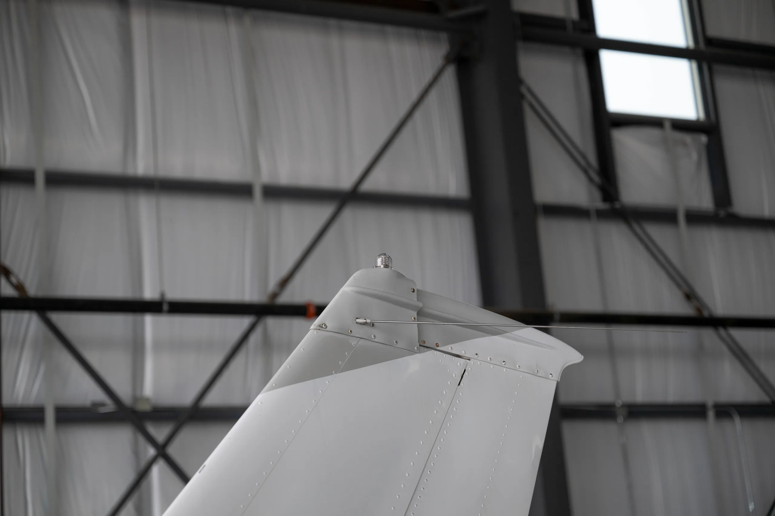 A close-up view of the vertical stabilizer and beacon light of a white aircraft in a hangar.