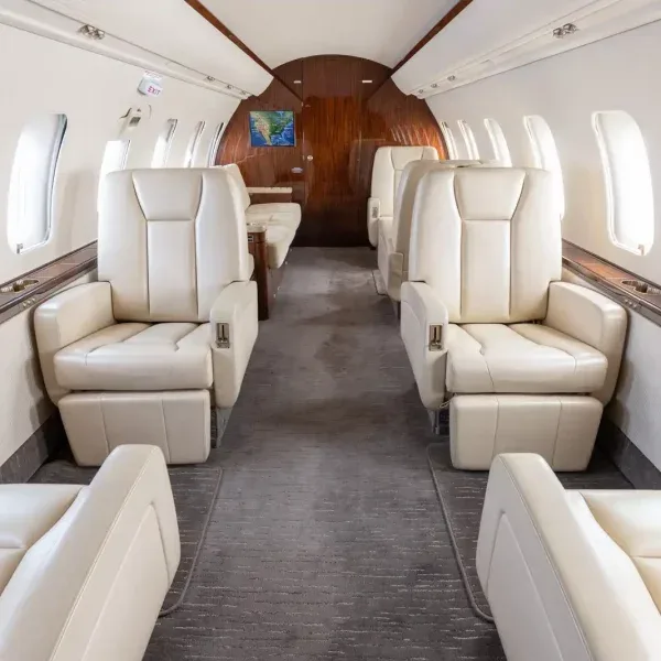 Interior view of a private jet cabin with light cream leather seats and a map display at the rear.