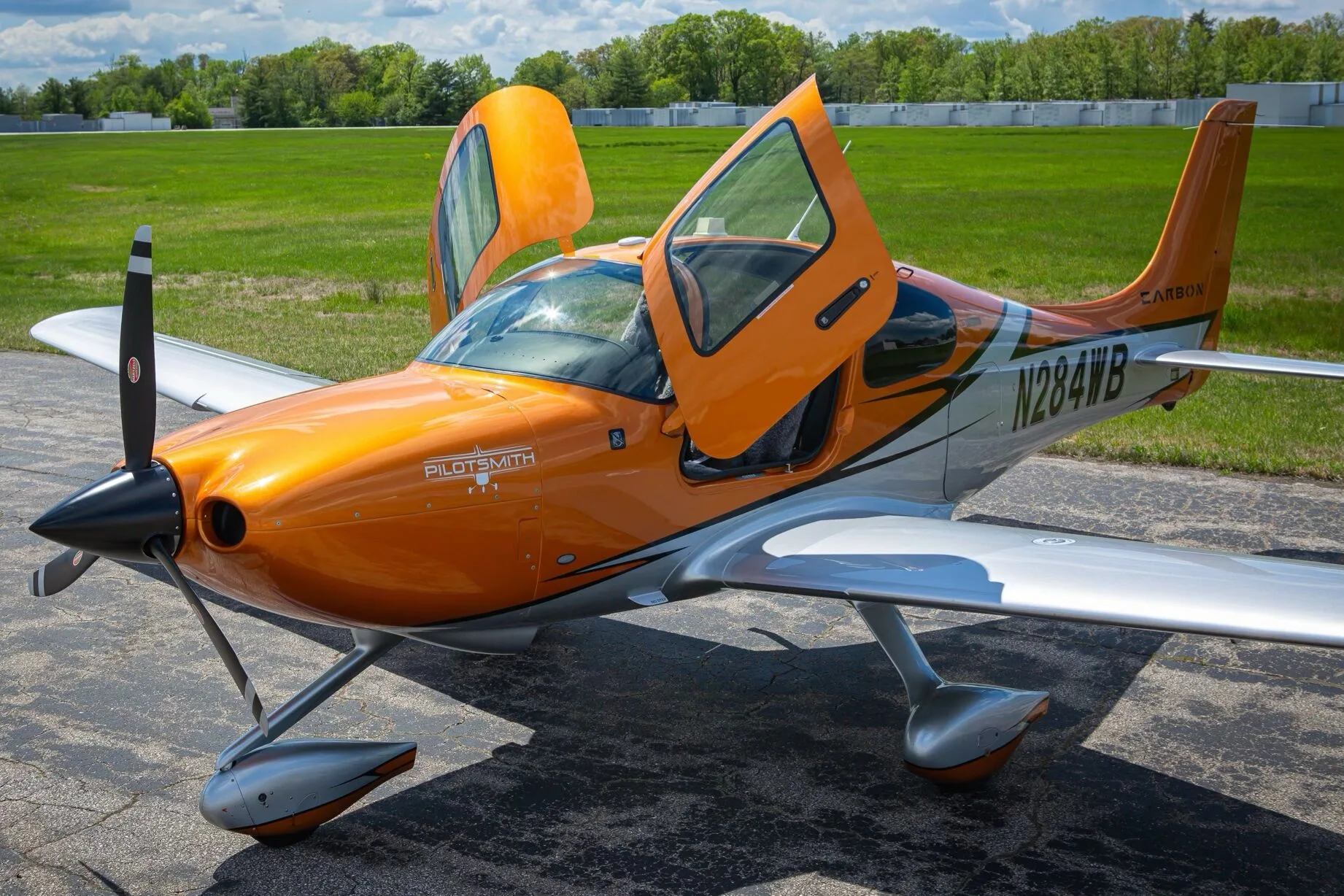 An orange and silver Cirrus SR20 aircraft, N284WB, with its gull-wing doors open on an airfield.