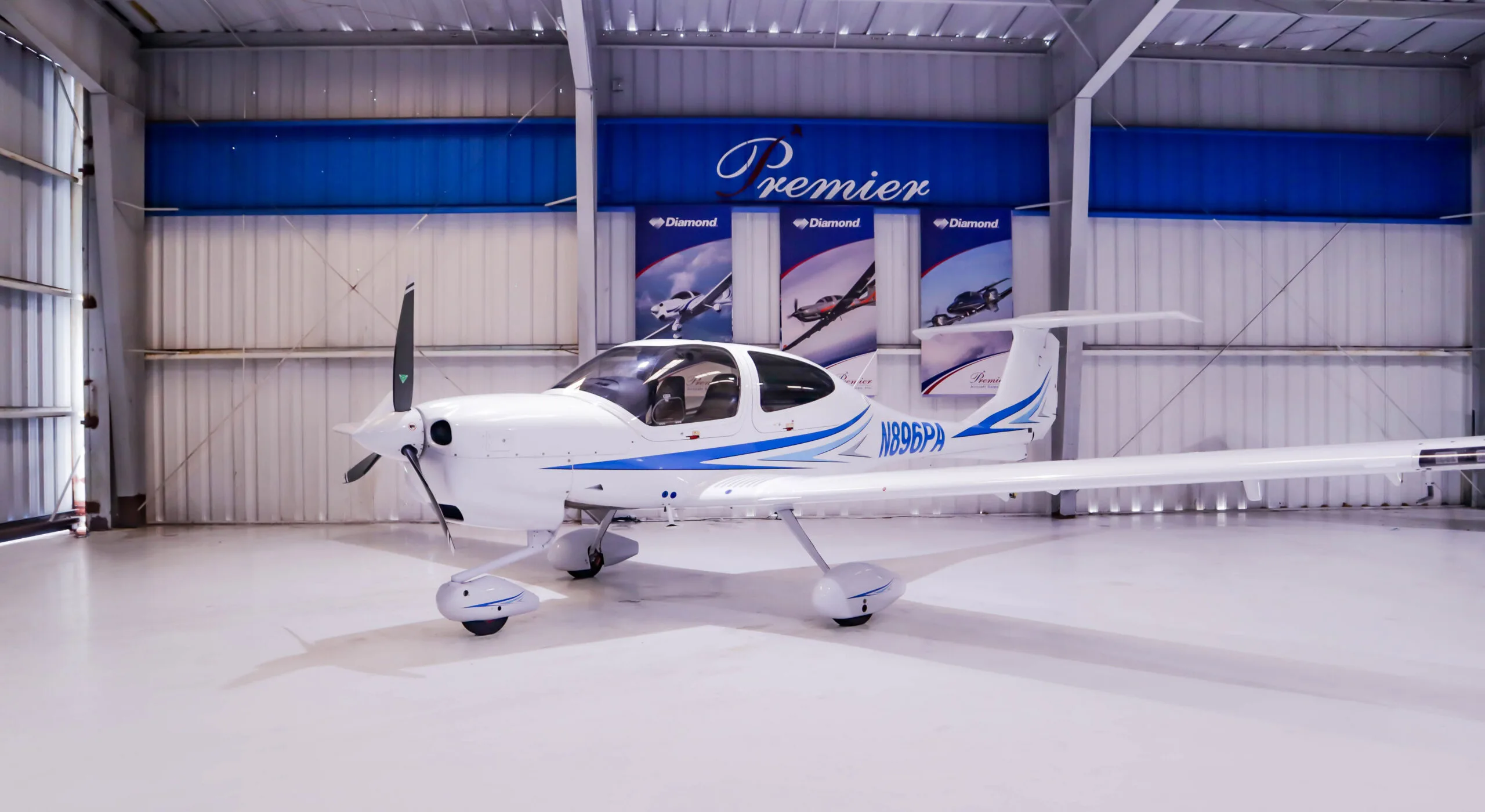 A white Diamond DA40 aircraft with blue stripes, registration N896PA, parked inside a hangar.