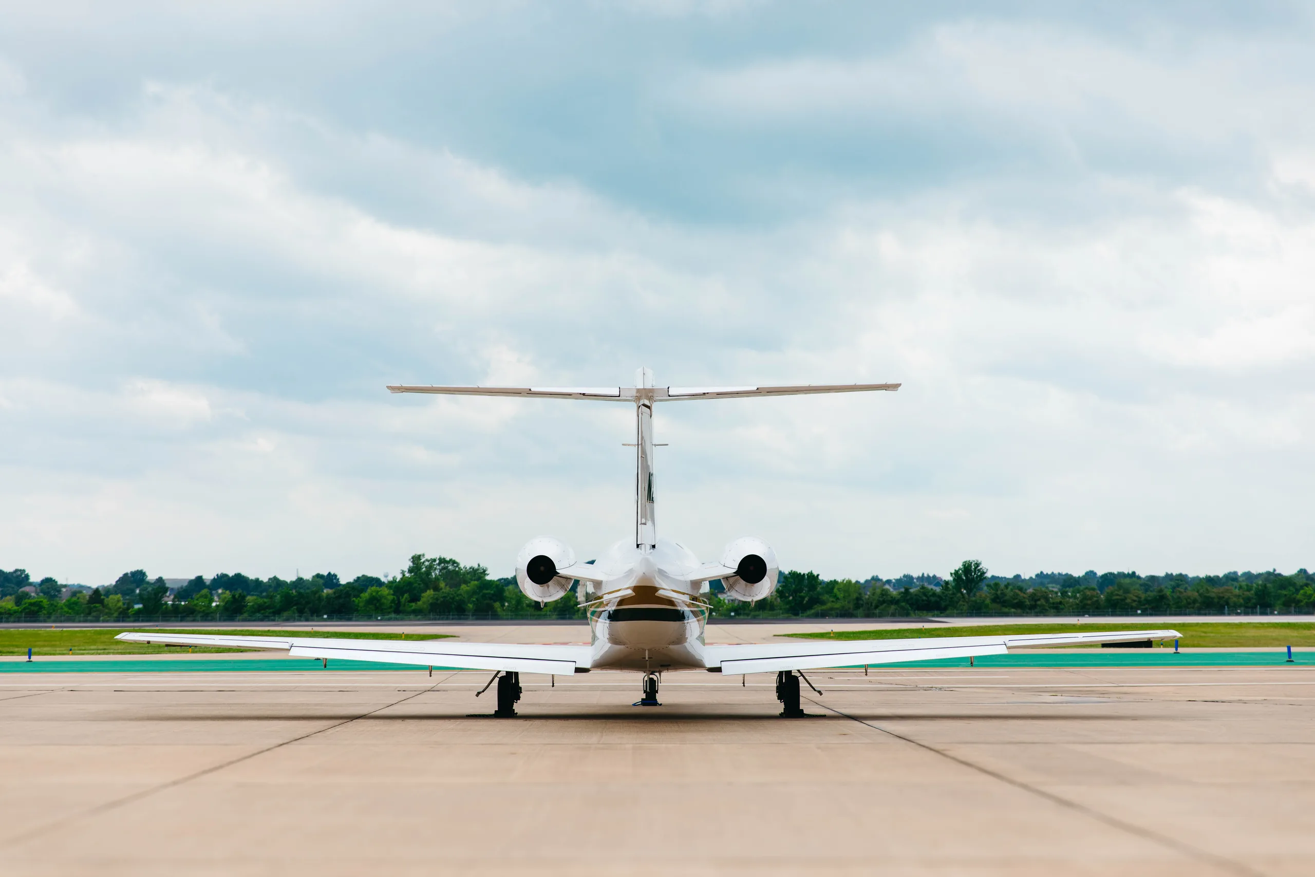 A rear view of a white Cessna Citation M2 business jet, tail number N22EM, parked on an airport taxiway under a cloudy sky.