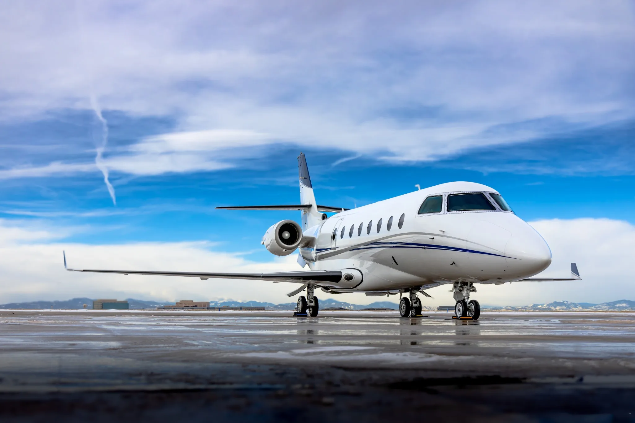 A white Gulfstream business jet with blue stripes parked on a wet tarmac under a blue sky.