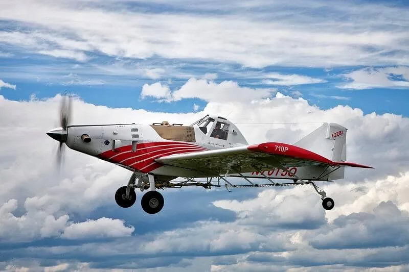A white and red agricultural aircraft with registration N701SQ flies against a blue sky with white clouds.