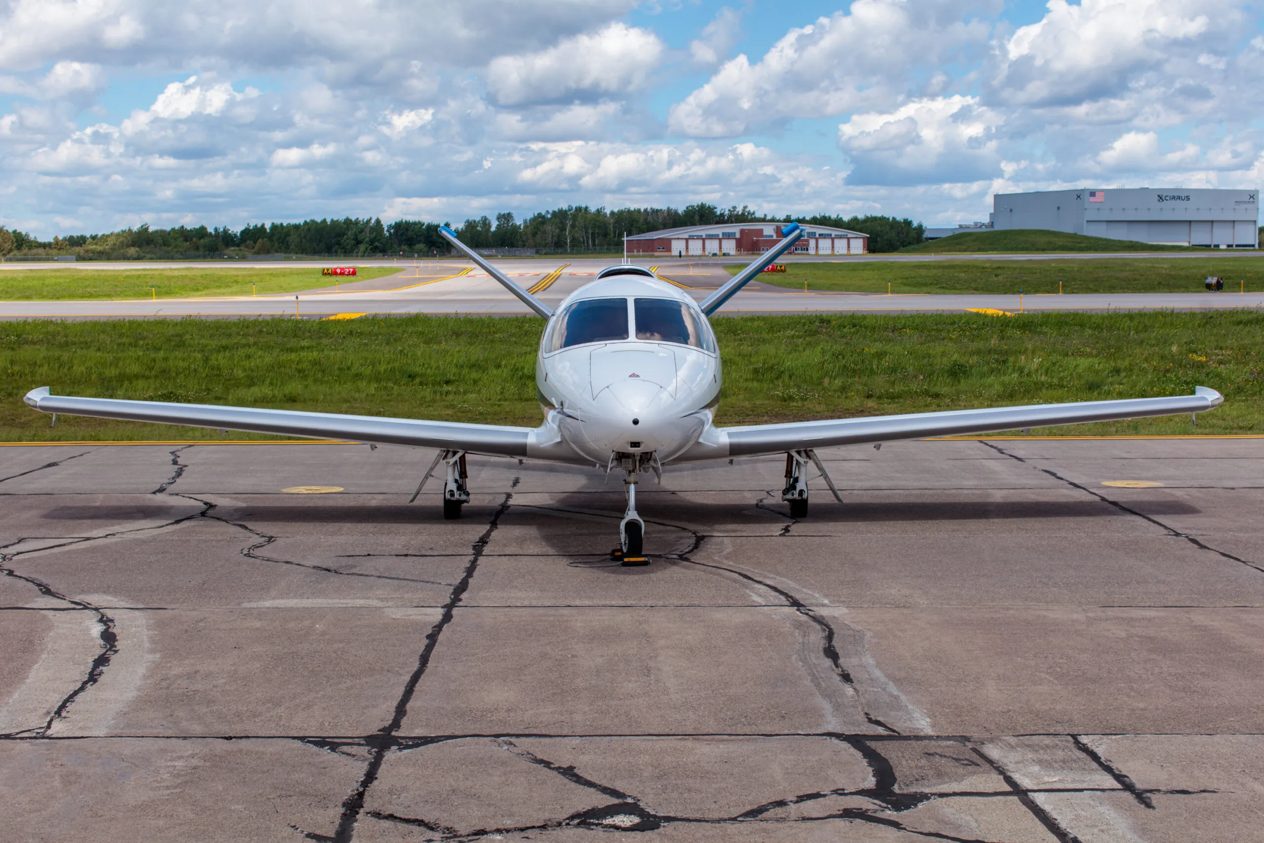 Front view of a white Cirrus Vision Jet (N218HP) parked on a tarmac with a hangar in the distance.