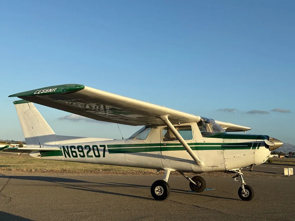 A white and green Cessna N69207 aircraft parked on an airfield with a clear sky.