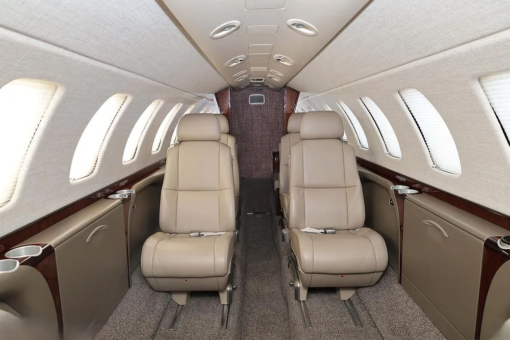 The aircraft's interior cabin shows beige leather seats and wood trim, looking towards the rear.