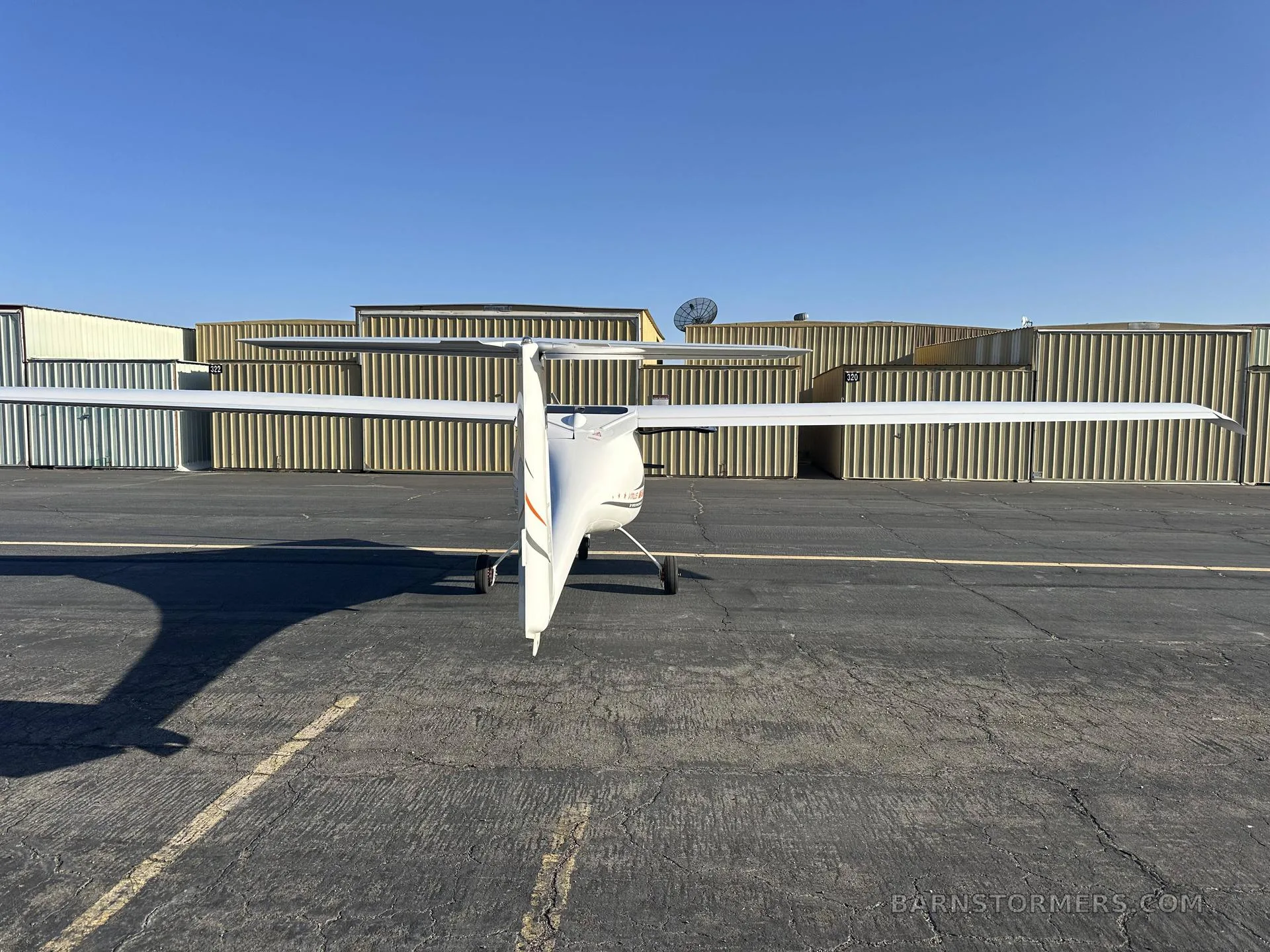 A white light sport aircraft, N442M, viewed from directly behind on an asphalt tarmac with hangars in the background.