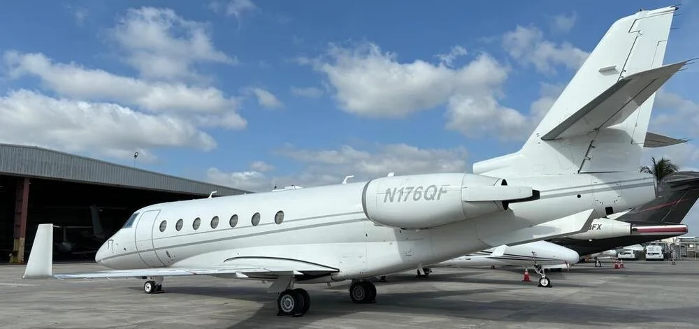 A side view of a white business jet, N176QF, parked on an airport tarmac next to a hangar.