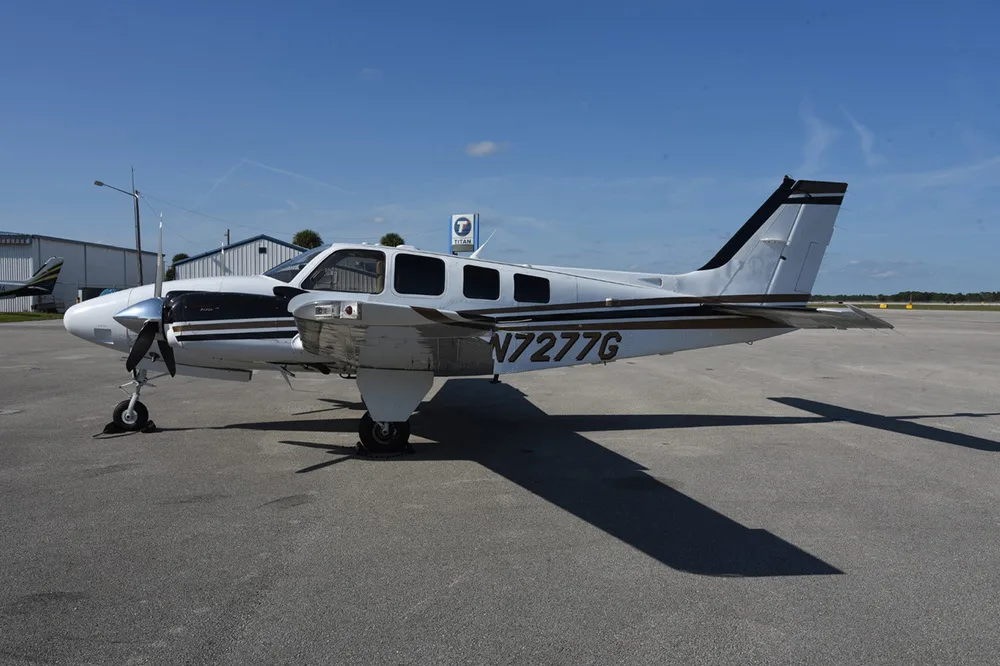 A white and black twin-engine propeller aircraft, N7277G, is parked on an asphalt tarmac under a clear blue sky.