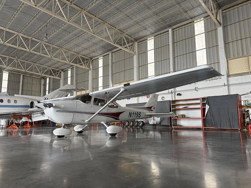 A white Cessna N119S with maroon accents is parked in a hangar, viewed from the front-left.