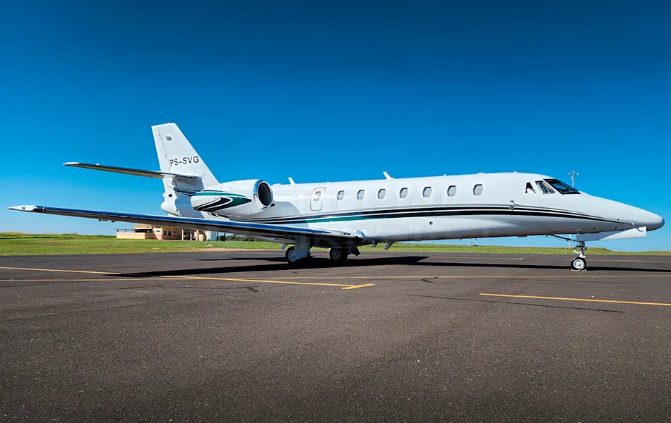 A white business jet with green and black stripes is parked on a tarmac under a clear blue sky.