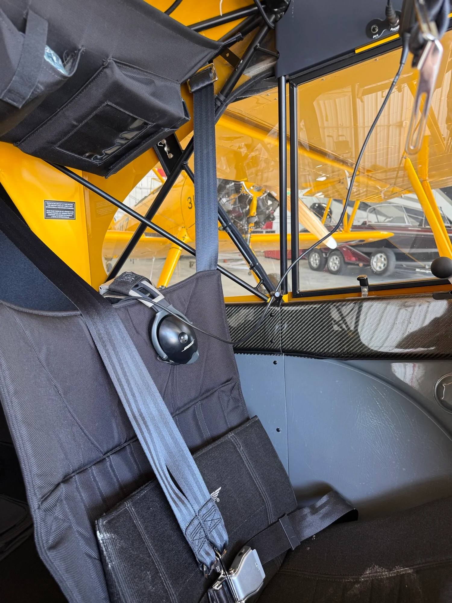 The black fabric seat and interior of a CubCrafters Carbon Cub EX-3, with a view of another yellow aircraft outside the window.