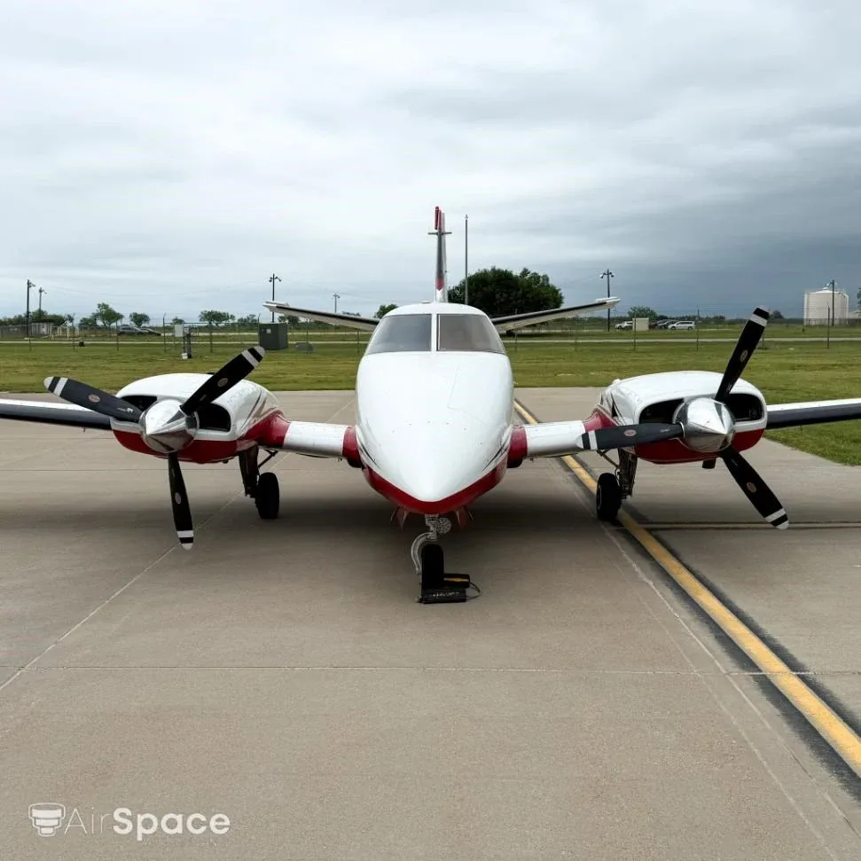 Front view of a white and red Beechcraft Duke N2889W parked on a tarmac under a cloudy sky.