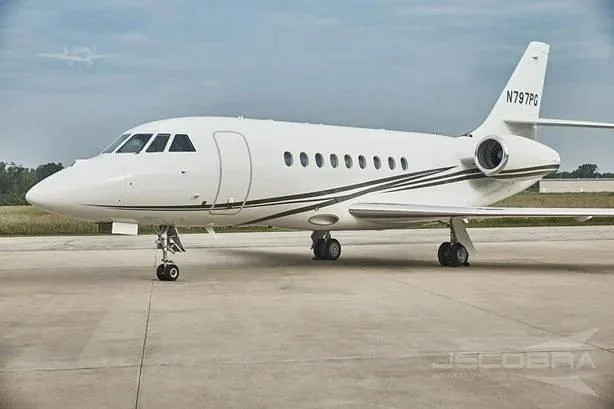 A white Dassault Falcon 900 business jet with black stripes, tail number N797PG, parked on a tarmac.