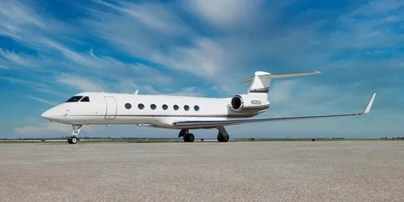 A white Gulfstream G550 business jet with silver accents is parked on a tarmac under a blue sky.