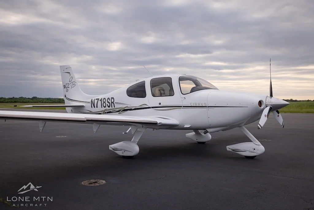 White Cirrus SR22T aircraft with black and gold accents parked on an asphalt tarmac under a cloudy sky.