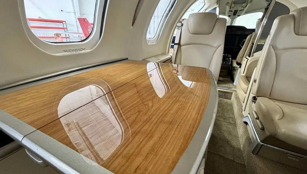 A close-up view of a wooden table and a beige leather seat in the aircraft's cabin.