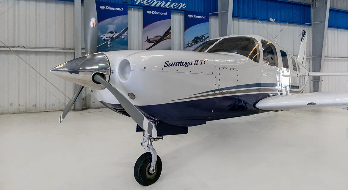 A close-up front view of the nose and propeller of a white and blue Piper Saratoga II TC aircraft.