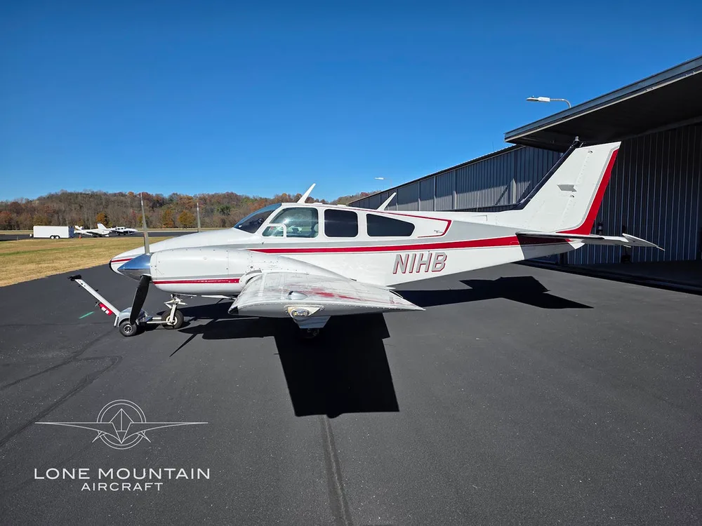 A side view of the white and red twin-engine aircraft, N1HB, parked on an airfield.