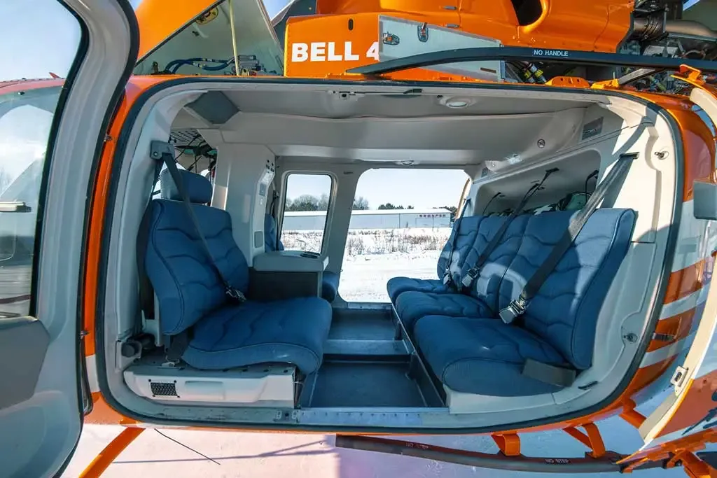 The helicopter's cabin interior with blue seats and an open door, showing the snowy exterior.