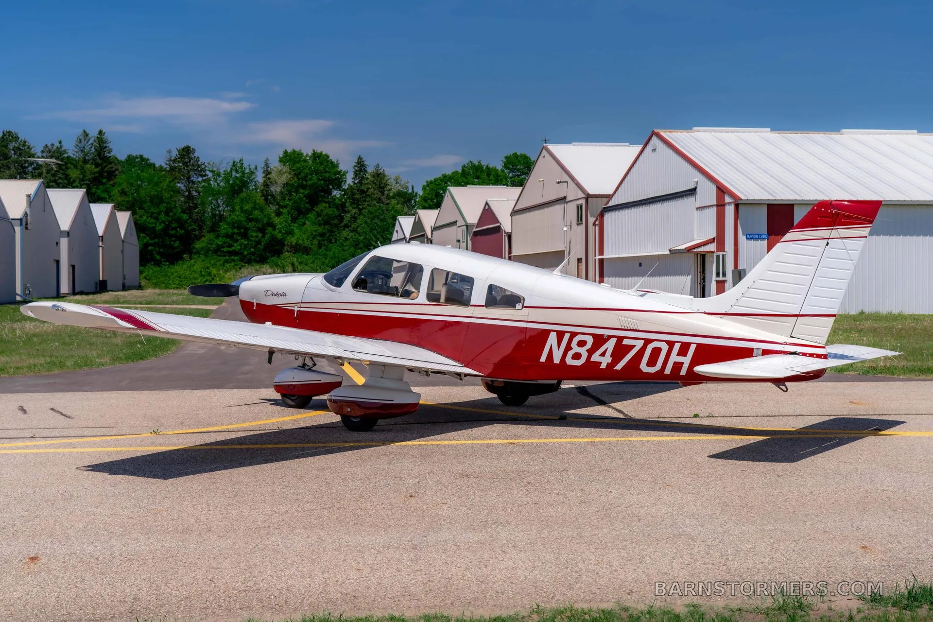 A red and white Piper Dakota aircraft with registration N847OH is parked on an asphalt tarmac with multiple hangars in the background.