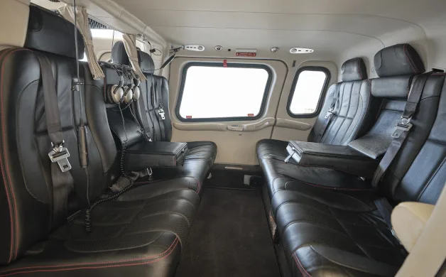 The luxurious black leather interior cabin of a helicopter, featuring multiple passenger seats with red stitching and headphones.