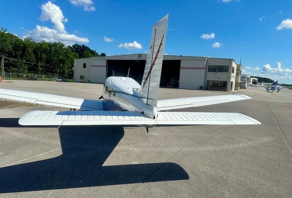 A rear view of the white Piper Saratoga II TC aircraft, N401BP, showing its tail and wings, parked on an airfield.