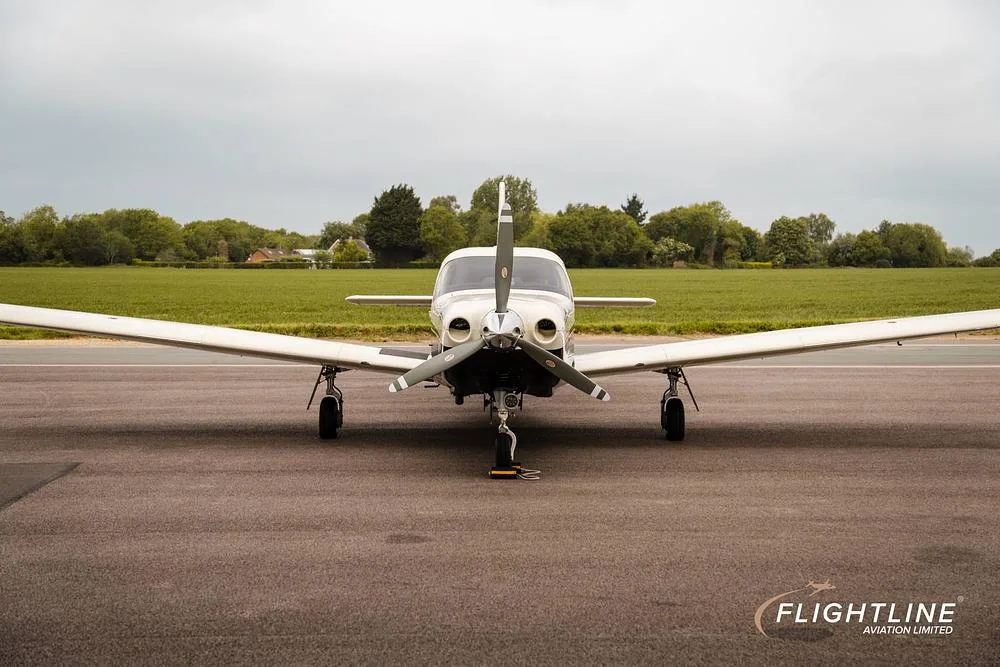 A head-on view of a white and black Piper Saratoga II TC, registration N446SE, parked on an asphalt runway.