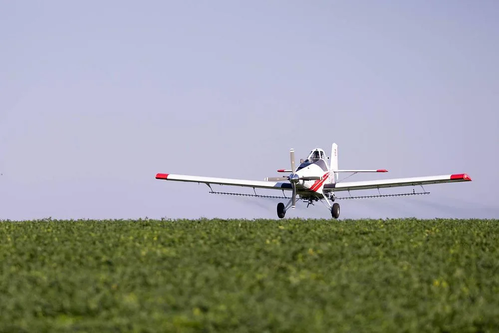 A white and red crop duster aircraft on a green field under a clear sky.