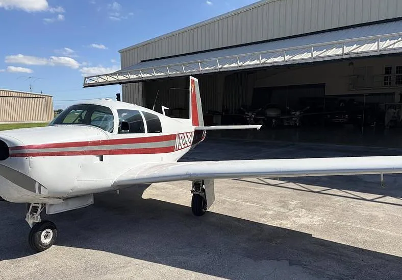 A white single-engine aircraft with red stripes, registration N9292M, parked outside a hangar.