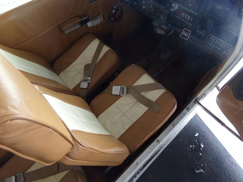 An overhead view of the tan and white leather interior seats of an aircraft, with a partial view of the cockpit instruments.