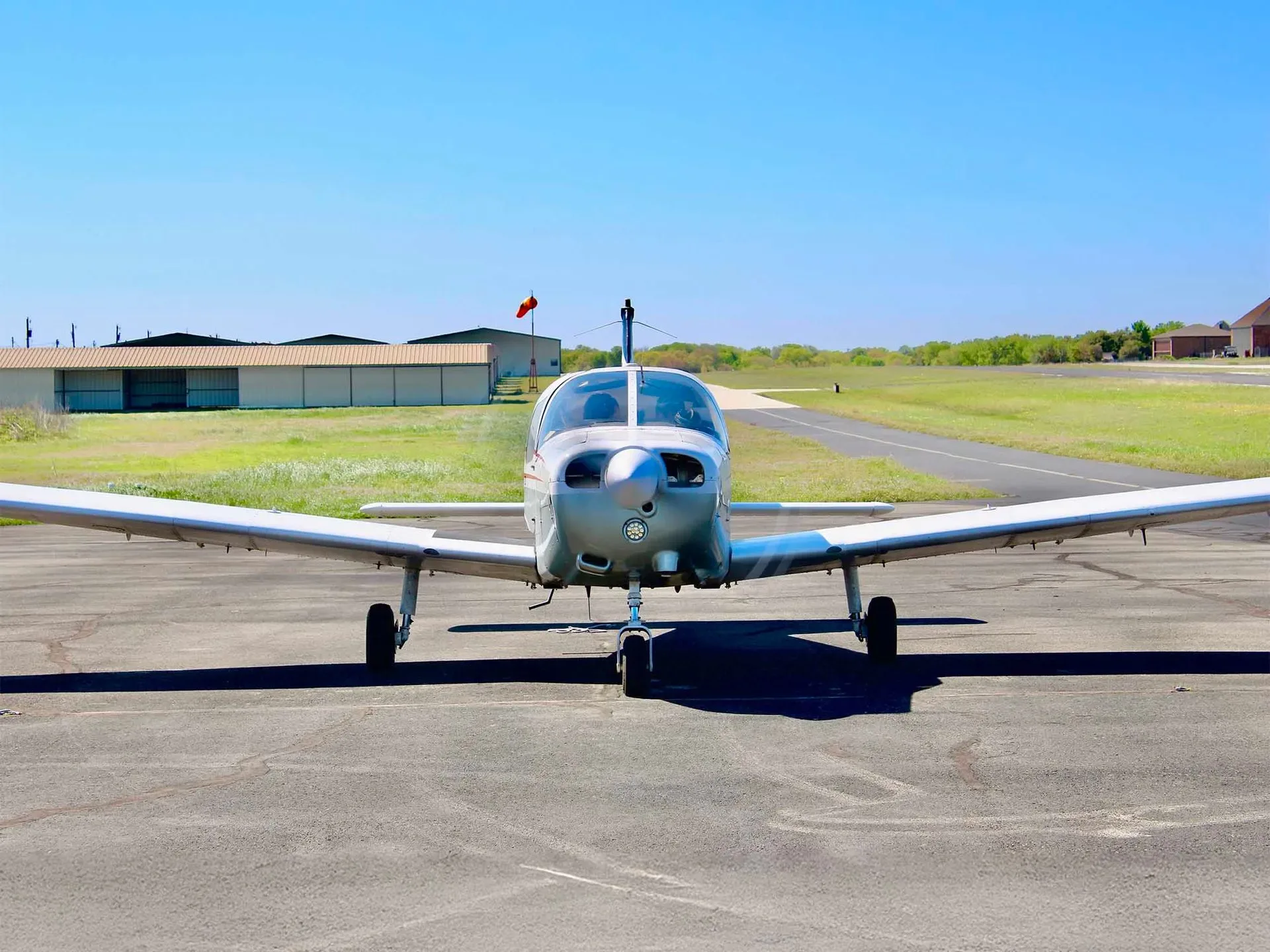 A silver single-engine aircraft parked on an asphalt runway under a clear blue sky.