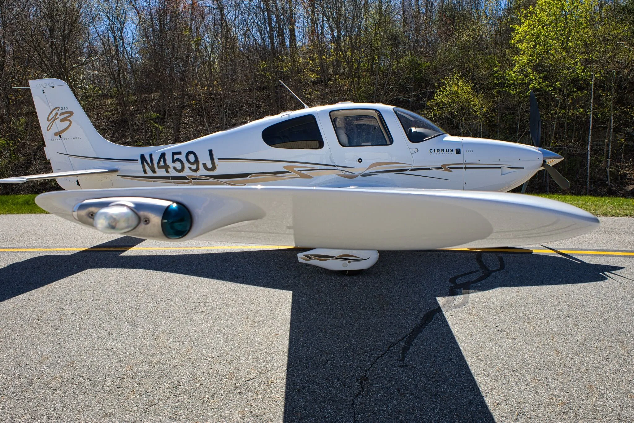 A close-up side view of the white Cirrus SR22 GTS Generation Three aircraft (N459J) with gold and black stripes, parked on an airfield.