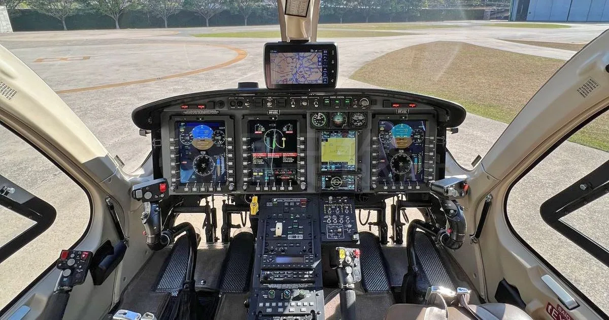 The cockpit of a helicopter featuring multiple digital displays and controls, looking out onto an airfield.