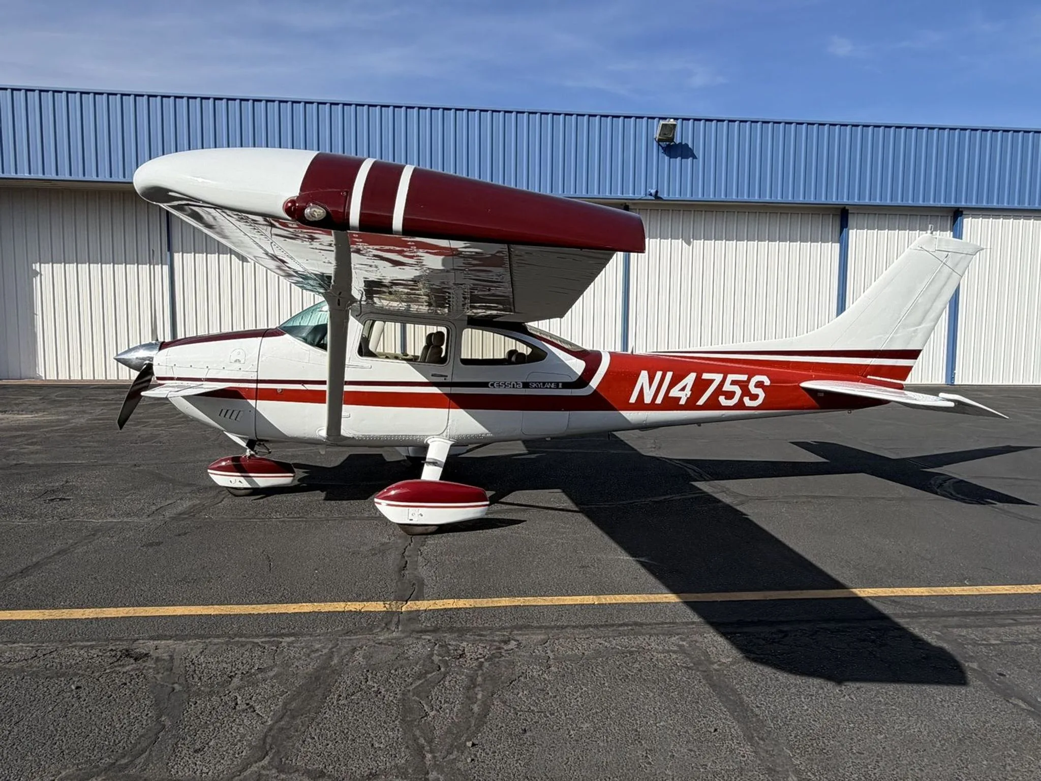 A white and red Cessna Skylane II (N1475S) parked on an airport tarmac, viewed from the front-left.