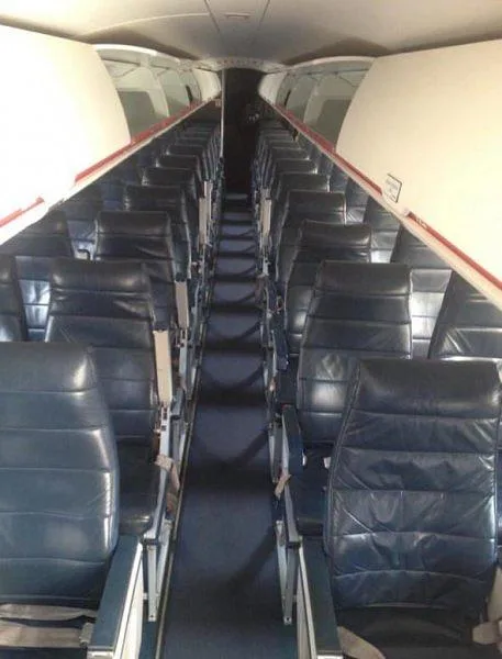 The interior cabin of an aircraft showing rows of dark blue leather seats and overhead bins.