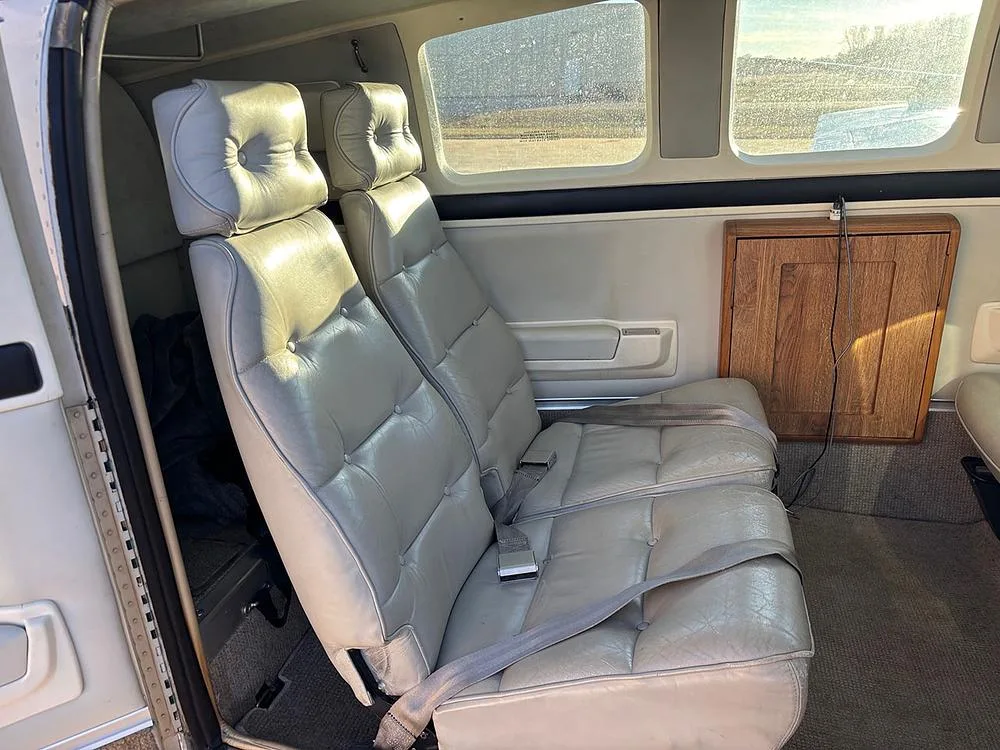 A row of two light grey leather passenger seats in the aircraft cabin with a wooden panel on the side.