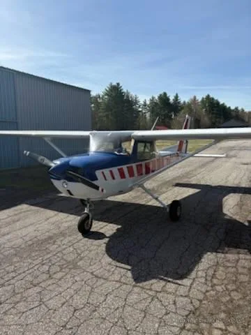 Front-right view of a white, red, and blue Cessna-style aircraft parked on a cracked tarmac next to a hangar.