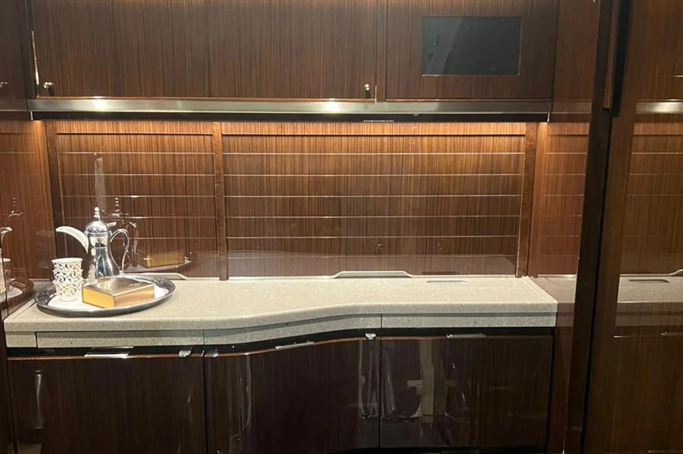A well-appointed galley area inside a private jet with dark wood cabinetry and a countertop.
