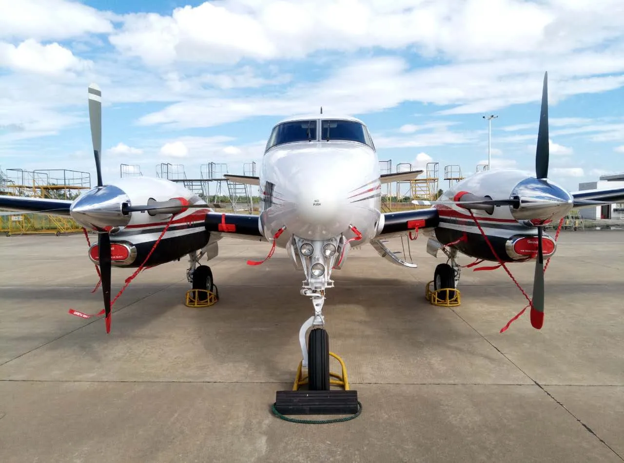 A King Air aircraft is parked on the tarmac with wheel chocks and propeller covers, front view.