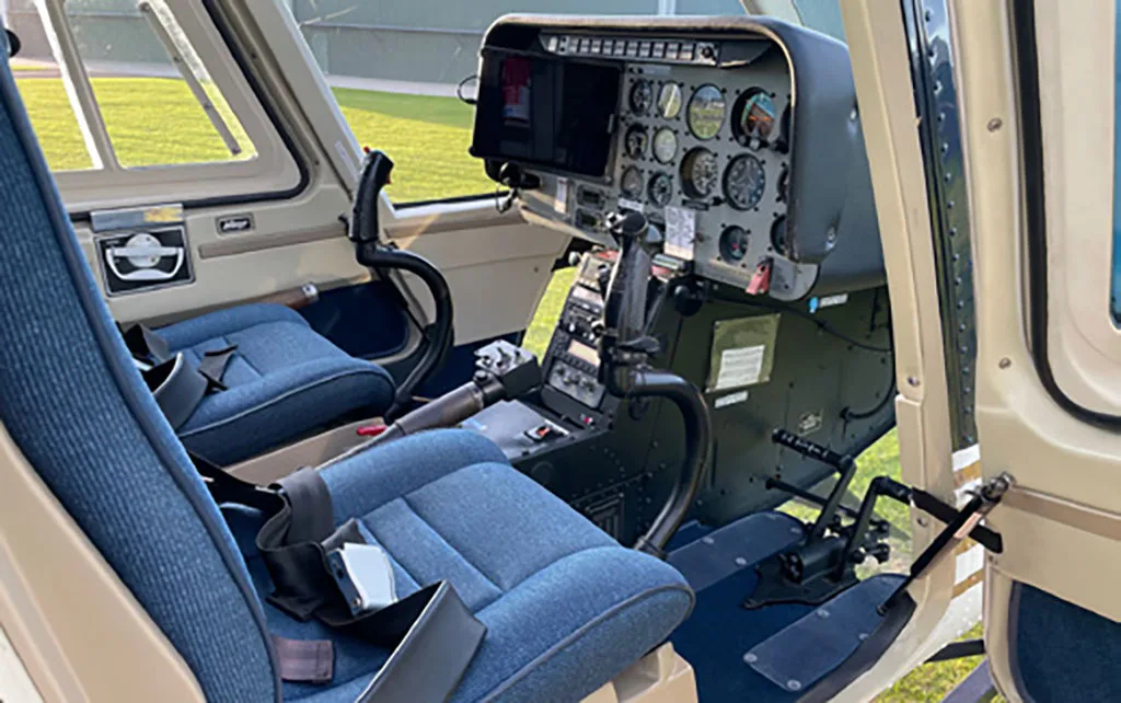 A wider view of the helicopter cockpit showing blue seats, control sticks, and the instrument panel.