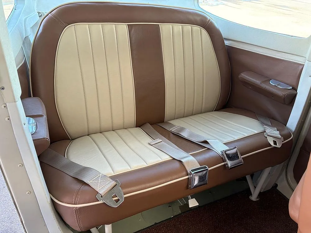 The rear bench seat of the aircraft, upholstered in two-tone brown and cream leather with seatbelts.