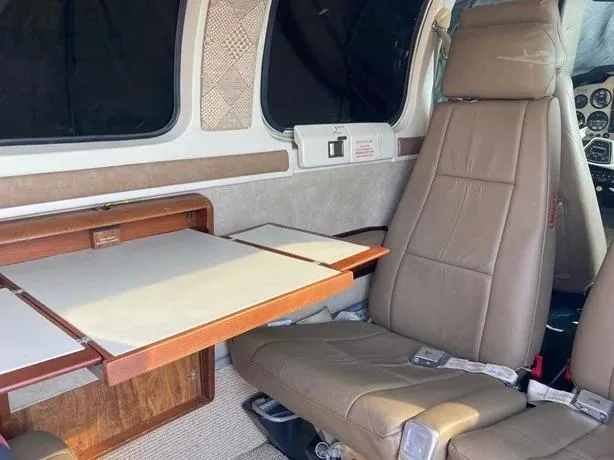 View of the aircraft's tan leather passenger seats and a wooden fold-out table in the cabin.